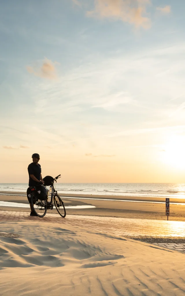 Cyclistes regardant le coucher de soleil sur la plage de Leffrinckoucke