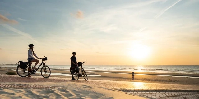 Cyclistes regardant le coucher de soleil sur la plage de Leffrinckoucke