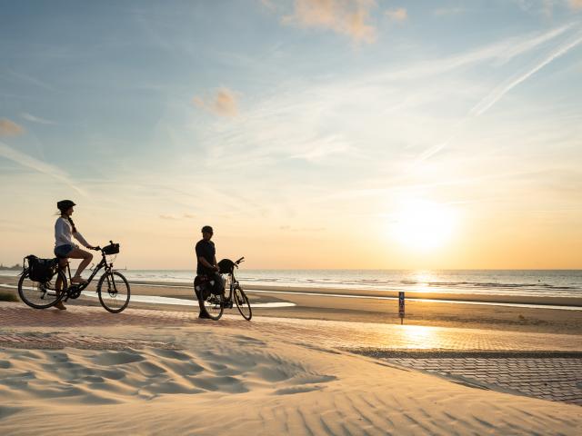 Cyclistes regardant le coucher de soleil sur la plage de Leffrinckoucke