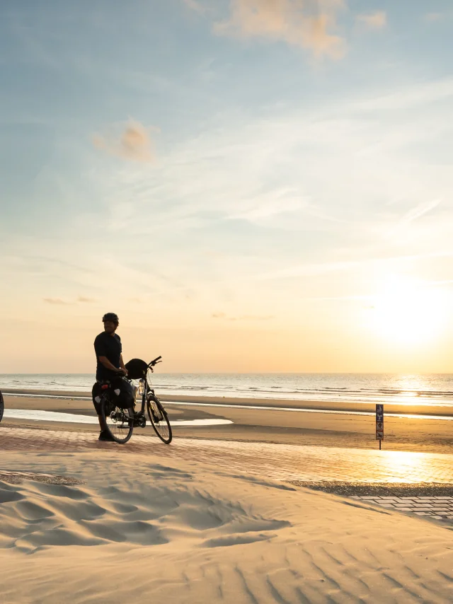 Cyclistes regardant le coucher de soleil sur la plage de Leffrinckoucke